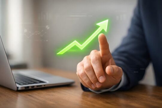 Businessman pointing at glowing green upward arrow showing financial growth and success