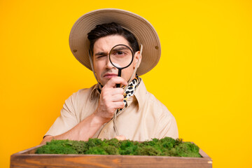 Male explorer with magnifying glass wearing safari hat examining moss in a wooden planter under a...