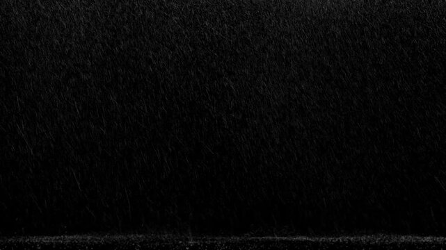 Wide shot of side windy rain with medium flow falling and landing on the ground with few bounces on a black background