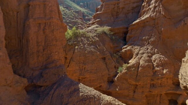 Low altitude drone flight between winding eroded sandstone canyon walls with sparse vegetation in Kyrgyzstan