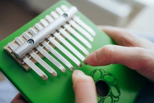 Close-up of hands playing a green kalimba, a modern version of the african mbira instrument, also known as a thumb piano, creating soothing melodies