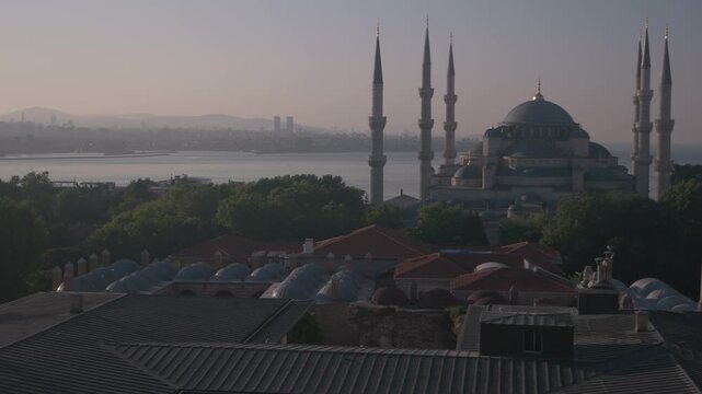 A wide view of Istanbul shows the Blue Mosque, rooftops, and distant skyline across the Bosphorus in soft morning light. Warm haze and layered landscape create depth and a peaceful atmosphere.