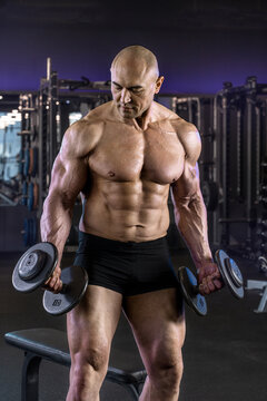 Muscular man holds dumbbells while posing confidently in a gym setting.