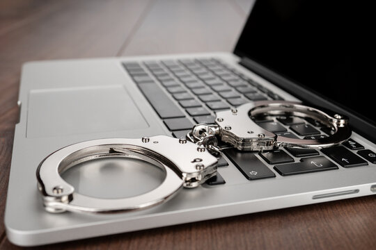 Closeup photo of handcuffs on modern laptop keyboard, symbolizing themes of restraint, cyber crime, justice and online security.