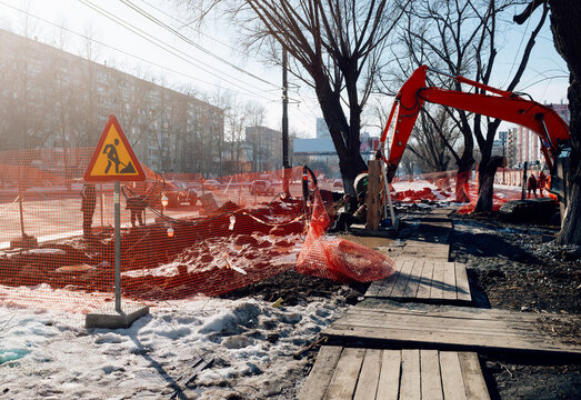 Excavator on the road. Road works on the street at spring city during the sunny day. Urban sidewalk construction with excavator