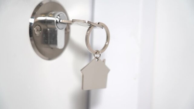 Key door house. A key in the door with a keychain in the shape of a house close-up. The concept of acquiring your own home. High quality FullHD footage