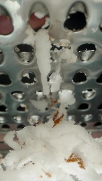 Vertical video. Grating Coconut Pulp on a Grater to Make Sweet Shavings, Macro View from a Low Angle, Under the Metal Mesh.