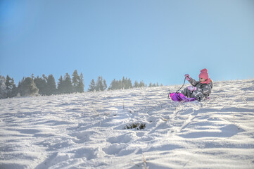 A joyful child sledging on a pink sledge, surrounded by a picturesque winter landscape, showing pure delight while enjoying the snow on a bright sunny day