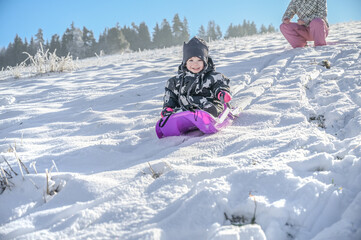 A young child sits relaxed on a bright sled, gazing innocently at the snowy landscape, capturing the essence of childhood wonder and joy in winter