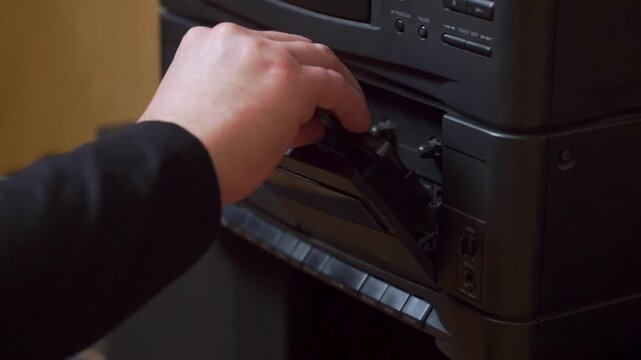 Male hand inserting audio cassette tape into old fashioned recorder, pressing turn on button and playing the music