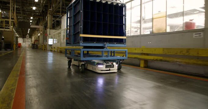 Autonomous mobile robot transporting a heavy blue cargo rack through a large industrial warehouse facility