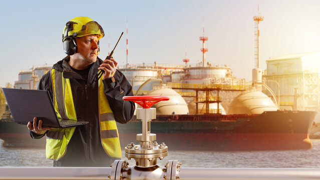 Oil and gas terminal operations. Industrial worker with helmet communicates by radio while monitoring pipeline valve and LNG tanker, symbolizing energy infrastructure, safety control,  fuel logistics.