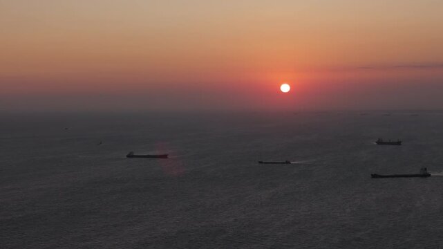 Aerial dolly out from ocean sunset with cargo ships silhouettes and fading orange sky, cinematic pull back revealing vast seascape