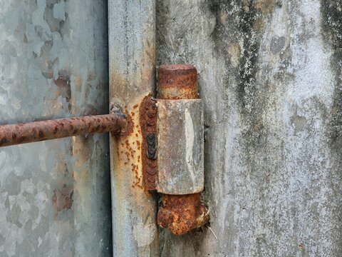 Closeup of rusty metal hinge on old gate showing corrosion and weathered industrial texture detail