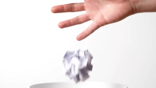 Hand holding crumpled paper over trash can.