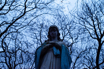 Fototapeta premium Sculptures on a grave against the background of tree branches in autumn at the old military cemetery Powązki, necropolis of Warsaw