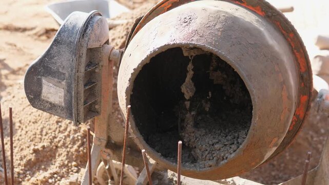 Rotating Concrete Mixer Positioned On Construction Site Near Formwork And Rebar, Drum Interior Visible With Fresh Mix, Operator Preparing Batch For Pouring Into Foundation Forms