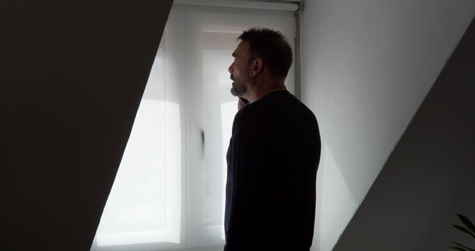 Contemplative Man Near Window: A man is lost in thought near a sunlit window. The soft light highlights his face as he considers the view, inviting viewers to ponder the moment.