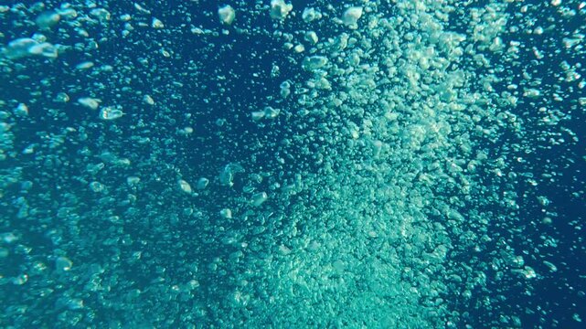 Motion of air bubbles popping up to surface against deep blue sea. Top view of rising curtain of air bubbles in bright daylight. Natural underwater background with bubbles of gas flows from depth