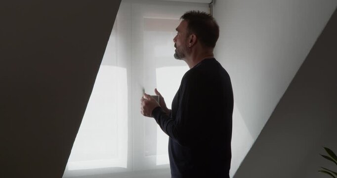 Contemplative Man Gazing: A man looks pensively toward a bright window, bathed in soft, diffused light, evoking a sense of introspection and thoughtful reflection.