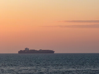 Obraz premium Container Ship Silhouette on Ocean Horizon During Golden Hour Sunset
