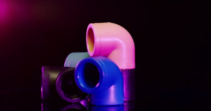 Group of colorful plastic elbow pipe fittings and industrial connectors against a dark background with red light