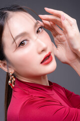 Fototapeta premium Elegant Asian woman in red fashion outfit posing in studio, showcasing beauty, confidence and modern style, flawless skin with bold makeup, luxury portrait highlighting feminine strength and glamour.