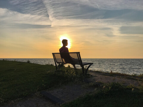 Silhouette of a man sitting on a bench, quietly watching a golden sunset over the sea. Warm light reflects across the water, creating a calm and timeless travel atmosphere, with a sense of solitude.