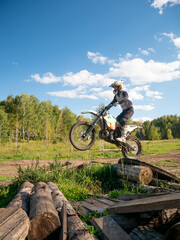 Motocross rider jumping on motorbike over log obstacle in field. Athlete practicing extreme sport on motorcycle. Off-road racing competition, speed, adventure and adrenaline concept. © Olesia Basova