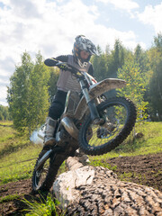 Obraz premium Motocross rider performing wheelie over fallen tree log in forest. Man racing dirt bike on off-road terrain. Extreme sports activity, speed, adrenaline, skill and outdoor adventure ride.