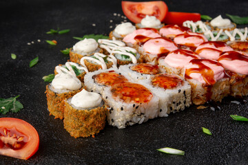 Assorted sushi rolls platter with pink creamy topping, spicy glaze, crispy maki and tomato garnish on dark stone background © Александр Гаврилычев