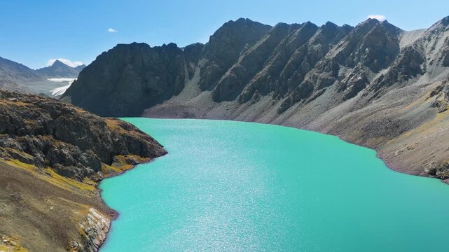 Drone flies above azure Ala Kul lake in Kyrgyzstan under clear blue sky in early Autumn