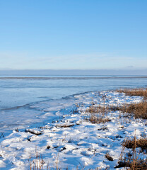 Naklejka premium Landscape, frozen and lake with ice in nature for climate change, winter season and morning frost. Space, blue sky and river with snow formation, freezing field and icy conditions from global warning