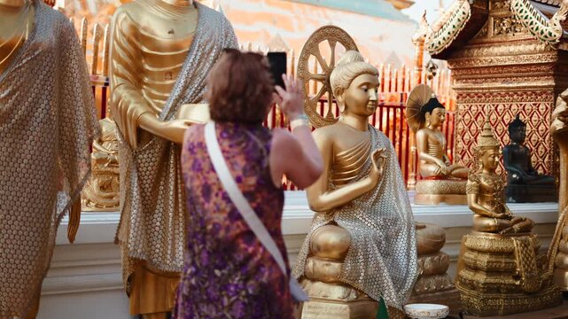 Tourist woman taking pictures of golden buddha statues at an ancient temple
