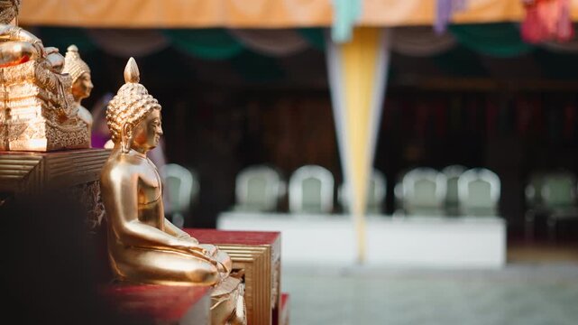 Golden buddha statues with tourists walking in a temple courtyard