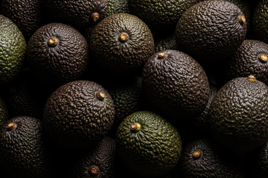 Full frame close-up of ripe Hass avocados piled together with dark moody dramatic lighting showing textured skin and stems