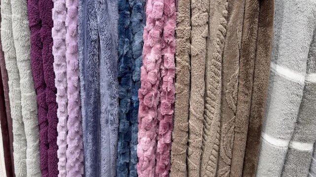 Variety of soft, fluffy, and colorful blankets hanging on display in a store, showcasing different textures, patterns, and hues for home decor and comfort, with price tags visible