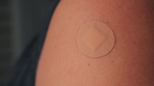 A close-up shot shows a small adhesive bandage placed on the shoulder after vaccination. The scene emphasizes healthcare, prevention, and personal responsibility. High quality 4k footage