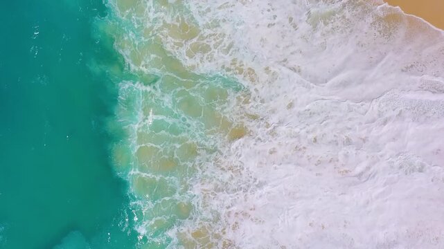 Aerial drone footage of massive turquoise waves crashing on a sandy tropical beach. Top view of powerful ocean surf and blue sea water. Concept of nature power, travel destination and summer.