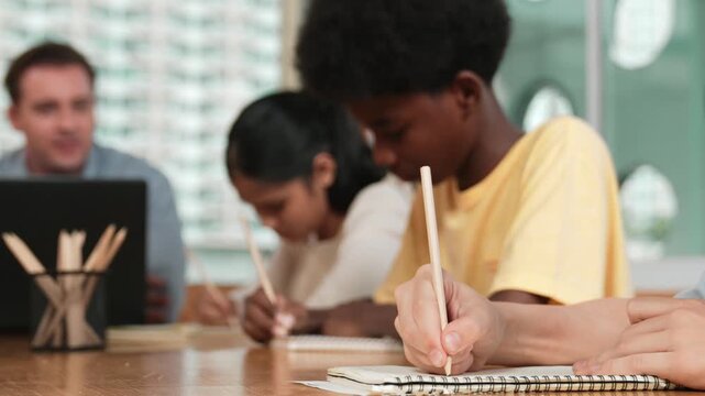 Closeup of student hand taking a note while girl ask teacher a question. Diverse student learning and study with smart happy instructor in classroom. Focus on hand. Creative education. Edification