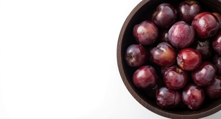 Obraz premium Ripe plums arranged in a dark wooden bowl on a clean white background
