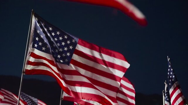 Close American flag motion at night in Malibu, California, USA illuminated by bright lights with fabric movement creating dramatic patriotic memorial atmosphere