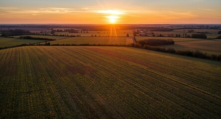 Fototapeta premium Expansive farmland with colorful crops seen from above during a glowing sunset
