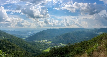 Obraz premium Scenic panoramic view of lush green mountain valleys under summer sunlight and dramatic clouds