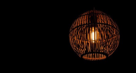 Obraz premium Dark interior background with a glowing wicker lamp chandelier highlighting woven rattan detail