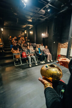 Performer Holding Handpan In Blackbox Theater, Dim Lighting And Tiered Seating With Attentive .