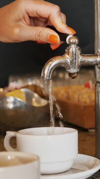 Close-up of female hand turning hot water tap and pouring boiling water into a tea cup