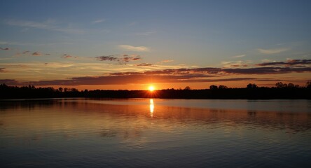 Obraz premium Golden sunset reflecting over calm water under a blue sky