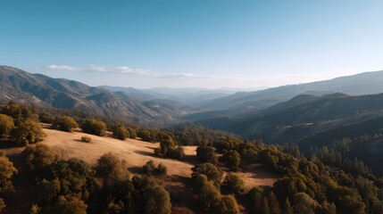 Obraz premium Serene mountain vista featuring rolling hills dense forests and deep valleys under a clear expansive blue sky