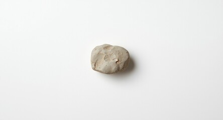 Fototapeta premium Single rock resting on a white smooth panel background with gentle daylight